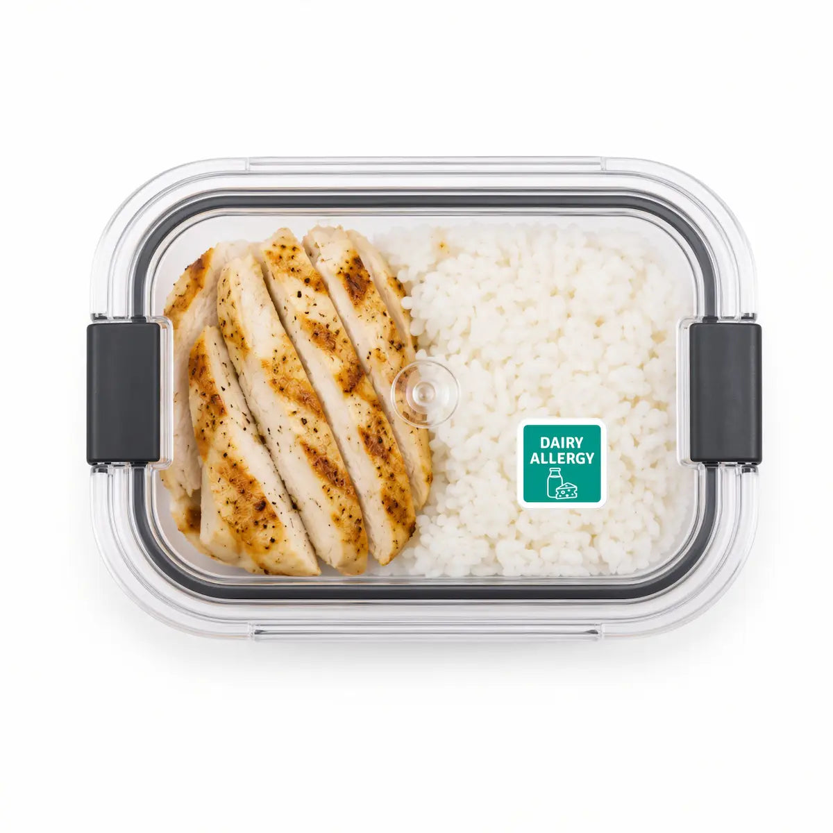 Clear plastic lunch box with a green dairy allergy warning sticker on the lid, containing sliced grilled chicken and white rice.