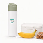 A cartoon milk carton dairy allergy alert sticker on a white kids’ water bottle beside a lunch container, banana, and pretzels, promoting milk allergen awareness for school lunches.