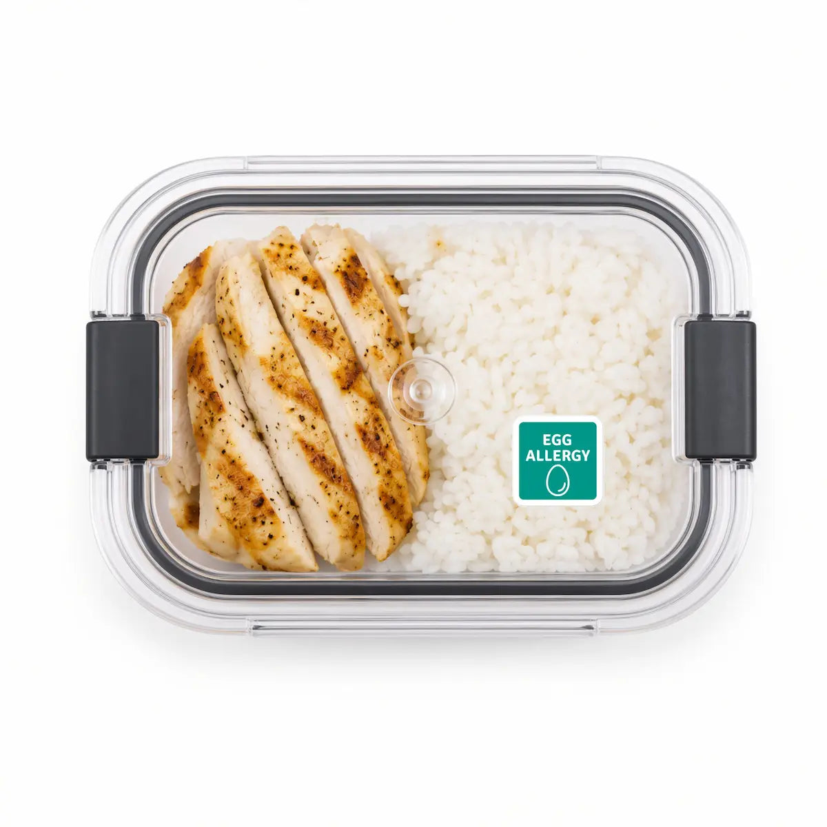 Clear plastic lunch box with a green egg allergy warning sticker on the lid, containing sliced grilled chicken and white rice.