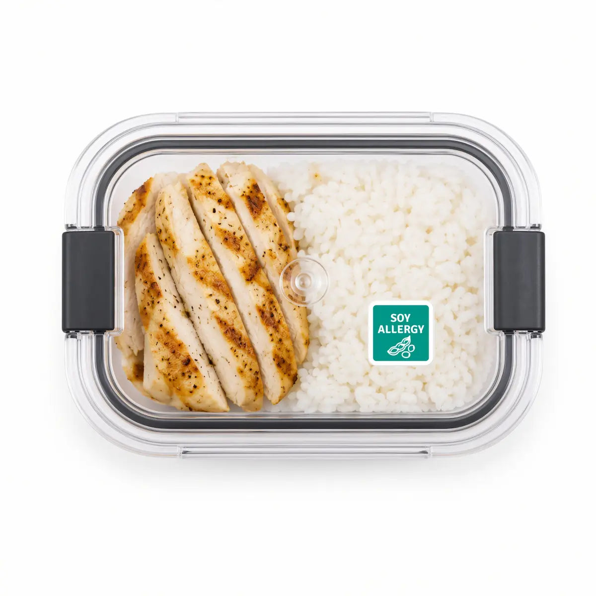 Clear plastic lunch box with a green soy allergy warning sticker on the lid, containing sliced grilled chicken and white rice.
