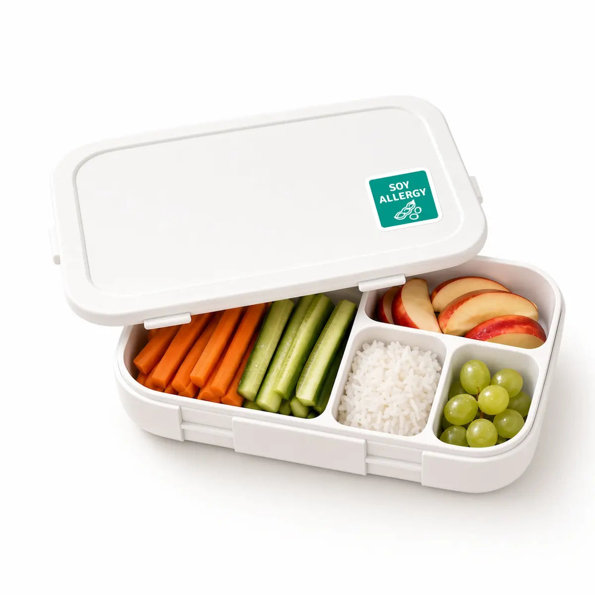 Open white lunch box with a green soy allergy warning sticker on the lid, containing a sandwich, apple slices, crackers, and green grapes